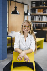 Portrait of a smiling young businesswoman sitting on a chair in loft office - GUSF03369