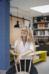 Portrait of a smiling young businesswoman sitting on a chair in loft office - GUSF03373