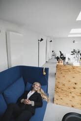 Lächelnde junge Geschäftsfrau auf Couch im Büro liegend - GUSF03386