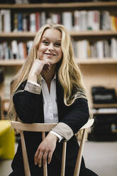 Porträt einer lächelnden jungen Geschäftsfrau, die auf einem Stuhl in einem Loftbüro sitzt - GUSF03429