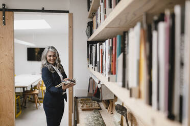 Smiling grey-haired businesswoman holding color samples in a loft office - GUSF03450