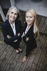 Portrait of smiling mature and young businesswoman standing on wooden terrace - GUSF03454