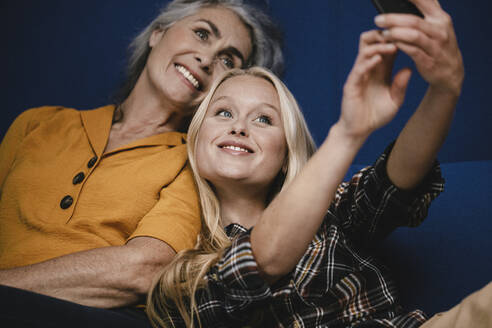 Glückliche Mutter und erwachsene Tochter machen ein Selfie auf der Couch - GUSF03468