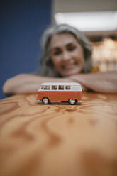 Grauhaarige Frau lehnt an einem Tisch mit einem Van-Modell - GUSF03479