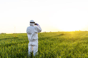 Wissenschaftlerin forscht im Feld und schaut durch ein Fernglas bei Sonnenuntergang - ERRF02772