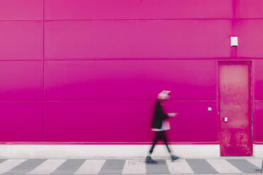 Young man with headphones walking along a pink wall, blurred - ERRF02782