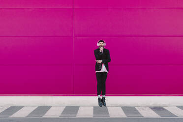 Young man using smartphone and listening to music, leaning on a pink door a - ERRF02786