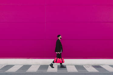 Junger Mann mit Reisetasche vor einer rosa Wand - ERRF02791