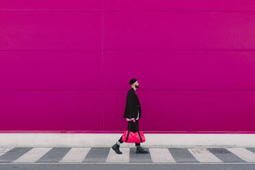 Young man walking with travelling bag in front of a pink wall - ERRF02791