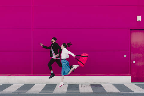 Mann und Frau laufen an einer rosa Wand entlang, lizenzfreies Stockfoto