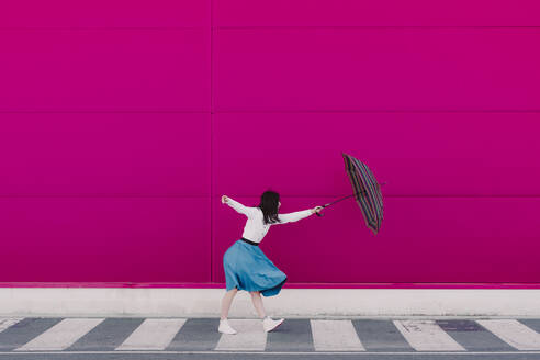 Junge Frau hält Regenschirm vor einer rosa Wand - ERRF02818