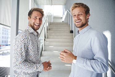 Portrait of two happy young businessmen at staircase - PNEF02359