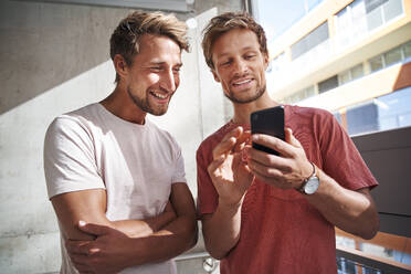 Zwei glückliche junge Männer teilen sich ein Smartphone - PNEF02385