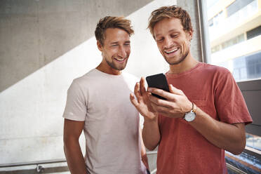 Zwei glückliche junge Männer teilen sich ein Smartphone - PNEF02386