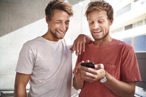 Two happy young men sharing smartphone stock photo