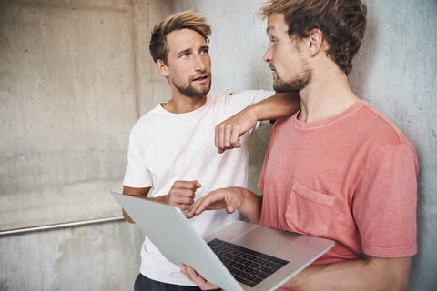 Two casual young men standing at a concrete wall using laptop stock photo