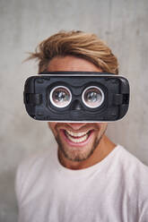 Laughing young man wearing virtual reality goggles - PNEF02418