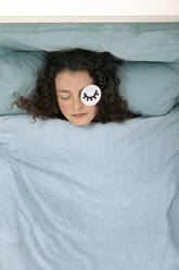 Porträt einer schlafenden jungen Frau im Bett liegend mit Papiermaske - PSTF00678