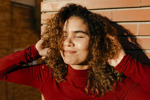 Portrait of young woman wearing red turtleneck pullover and enjoying sunlight - TCEF00216