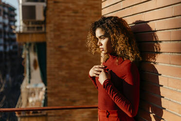 Portrait of young woman wearing red turtleneck pullover and standing on a balcony - TCEF00218