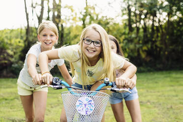 Glückliche Mädchen fahren Fahrrad im Garten - SODF00626