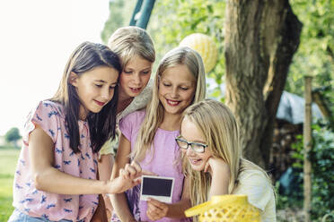 Happy girls looking at instant photo on a birthday party outdoors - SODF00650