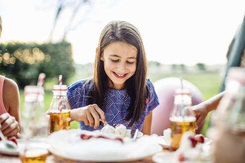 Glückliches Mädchen isst ein Stück Kuchen auf einer Geburtstagsparty im Freien - SODF00674