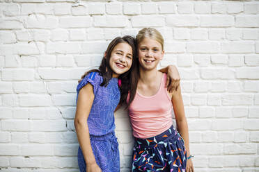 Porträt von zwei glücklichen Mädchen, die sich an einer Wand umarmen - SODF00682