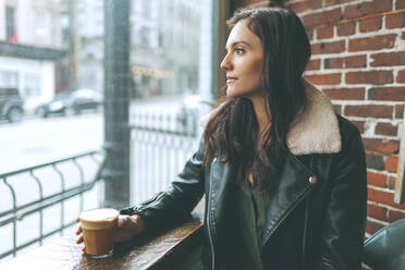 Frau mit einem Kaffee, die aus dem Fenster eines Cafés schaut - CMSF00091