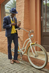 Stylish young businessman with bicycle wearing old-fashioned suit checking his phone - VEGF01615