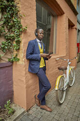 Stilvoller junger Geschäftsmann mit Fahrrad im altmodischen Anzug hört Musik über Kopfhörer - VEGF01619