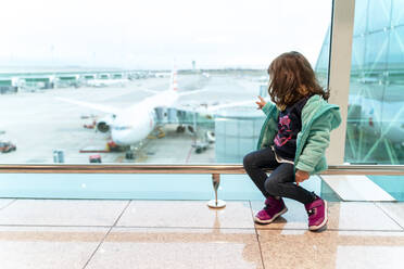 Mädchen, das auf dem Flughafen vor einem Flugzeug sitzt, bereit zu reisen - GEMF03466