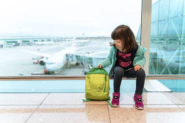 Girl with backpack sitting at the airport in front of a plane - GEMF03467