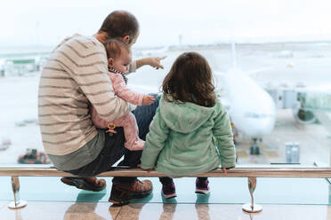 Vater mit zwei Töchtern auf dem Flughafen vor einem Flugzeug sitzend - GEMF03468