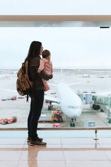 Mutter mit Baby und Rucksack auf dem Flughafen vor einem Flugzeug auf dem Flughafen in Barcelona, Spanien - GEMF03469