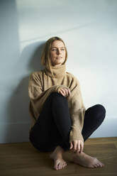 Porträt einer nachdenklichen blonden jungen Frau, die auf dem Boden sitzt - PNEF02435