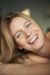 Porträt einer glücklichen blonden jungen Frau, die sich hinlegt - PNEF02440