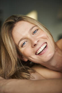 Portrait of happy blond young woman lying down - PNEF02440