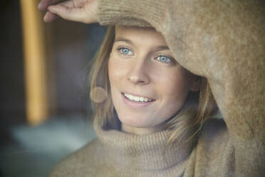 Porträt einer lächelnden blonden jungen Frau hinter einer Fensterscheibe - PNEF02448