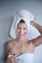 Portrait of happy young woman with her head wrapped in a towel - PNEF02449