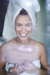 Porträt einer glücklichen jungen Frau, die ihren Kopf in ein Handtuch gewickelt hat - PNEF02450