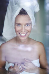 Portrait of happy young woman with her head wrapped in a towel - PNEF02450