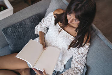 Junge Frau sitzt zu Hause auf der Couch und liest ein Buch - MPPF00523