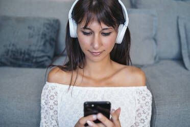 Porträt einer jungen Frau, die im heimischen Wohnzimmer mit Kopfhörern Musik hört - MPPF00528