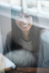 Porträt einer lächelnden jungen Frau hinter einer Fensterscheibe - MPPF00535