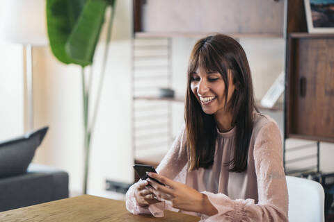 Glückliche junge Frau, die zu Hause ein Mobiltelefon benutzt, lizenzfreies Stockfoto