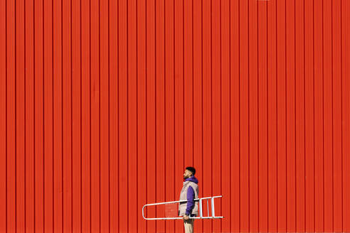 Junger Mann mit einer Leiter vor einer roten Wand - ERRF02821
