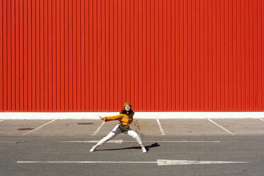 Young woman dancing in front of a red wall - ERRF02829