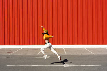 Young woman dancing in front of a red wall - ERRF02834