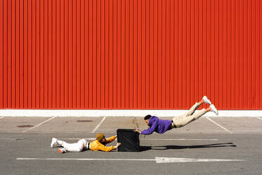 Young man and woman performing with a box in front of a red wall - ERRF02850